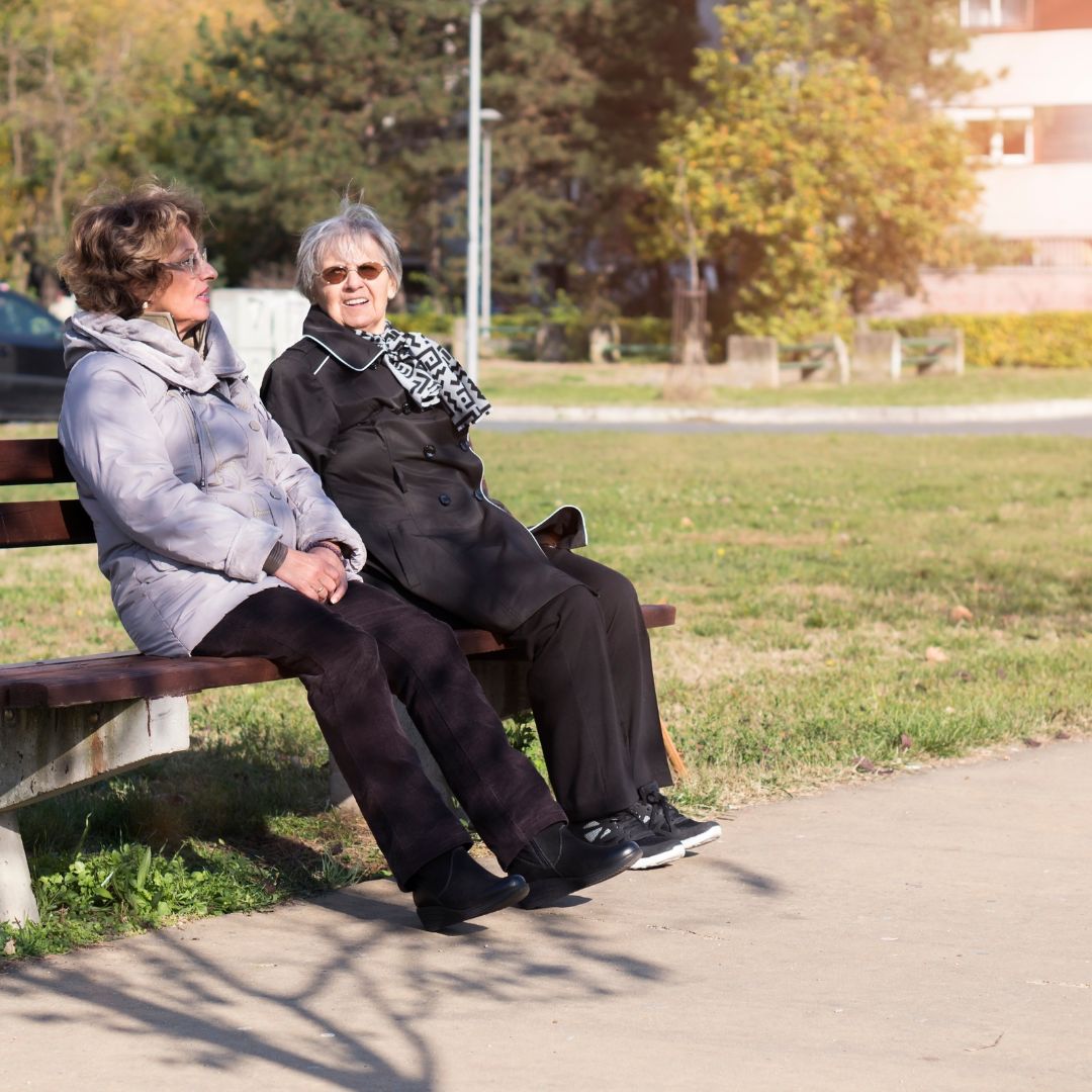 Two elderly women sitting on a bench together talking
